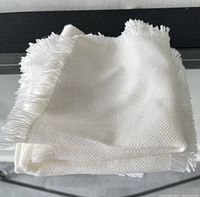 Stack of folded white cloth napkins showing texture and fringe edge detail.