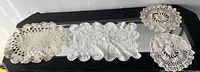 Photo showing four assorted vintage crochet doilies placed on a black surface with a mirror beneath.