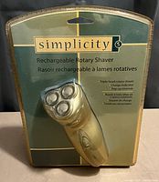 Front view of the Simplicity rechargeable rotary shaver in sealed retail packaging. Visible are the three rotary shaver heads and the brand information on the packaging.