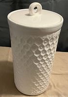 Tall white ceramic cannister with textured dot honeycomb pattern and looped handle lid.