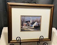 Full view of framed print showing a village scene with church steeple in the background, under glass with wooden frame.