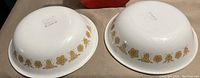 Two white Pyrex bowls with yellow floral design shown upside down to display markings.