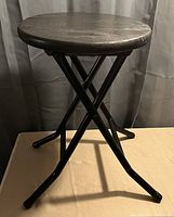Photo of a small round accent table showing a dark wooden top and black metal crossed legs.