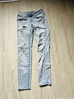 Full front view of light blue ripped jeans laid flat on floor showing distressed areas and pockets.