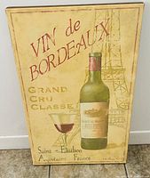 Photo of rectangular vintage style wall decor depicting a green Bordeaux wine bottle, filled wine glass, and faint Eiffel Tower with French text.