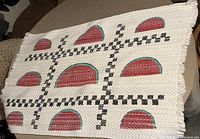 Photo of the woven kitchen mat with watermelon slice pattern and checkerboard design, showing its texture and fringed edge.