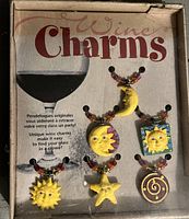 Original box of wine charms featuring a wine glass silhouette and text in English and French, with six different celestial-themed wine charms attached to beaded hoops.