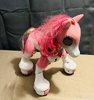 Plastic pink and white Zoomer toy pony with pink and brown hair mane, black grid eyes, mechanical leg joints, and roller wheels on each hoof for movement.