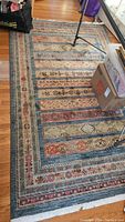 Full view of Persian style rug laid on hardwood floor with parts of furniture and a cardboard box at the corners.