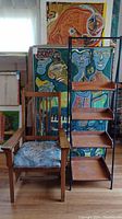 Both vintage wood mission armchair and 4-tier shelf unit placed side by side with colorful paintings in the background.