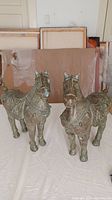 Front and angled view of two Chinese bronze horse sculptures on a table with paintings behind them.
