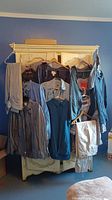 Men's pants and shirts hanging on hangers in front of white cabinet. Mixed colors mostly blue, grey, and beige.