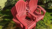 Four red plastic Adirondack chairs placed on grass, showing slatted backs and wide armrests typical of Adirondack style.