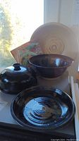 Photo showing a large beige pottery bowl, a small black glazed covered dish, a black glazed bowl, and a pottery plate.