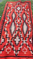 Full view of blanket laid flat showing red, cream, and black geometric diamond and cross pattern.