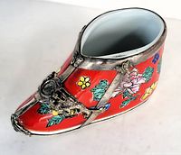 Front and right side angle of porcelain shoe figurine showing red floral painted design and silver mountings with clasp detail