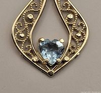 Close-up of filigree pendant with heart-shaped blue topaz centered