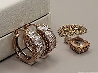 Close up of earrings and necklace pendant with chain on a light display stand, showing rose gold tone and clear stones.