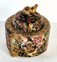 Top-down view showing the domed lid with a golden bird finial and detailed colorful floral and Asian figure painting on the jar.