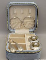 Velvet LA KAISER jewelry storage box open, showing three pairs of earrings: twisted hoop hoops hung inside lid; long water-drop clip-on earrings; two-tone hammered disc clip-on earrings with faux pearl in center in lower compartments.