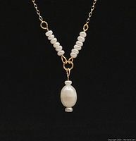 Close-up photo of the yellow gold necklace with integrated freshwater pearls on a black background.