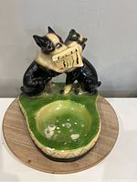 Top view of vintage ceramic ashtray with two black and cream Boston Terrier dogs holding a music sheet, on a green base with ash bowl showing wear