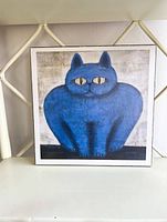 Square wall plak art of a blue cat placed on a white chair.