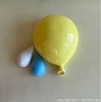 Photo showing the three ceramic wall balloons arranged together on a light background, highlighting their smooth glossy finish and colors (yellow, blue, white).