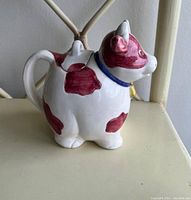Side view of the ceramic cow-shaped teapot showing reddish-brown patches and handle