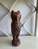 Front view of a wooden owl statue showing detailed carved feather and eye patterns on a smooth wood finish.