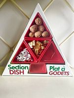The section dish set boxed in a triangular cardboard box displaying the four red ceramic dishes arranged in a Christmas tree shape with one green base plate. The dishes currently hold walnuts and some small chocolates to show serving use.