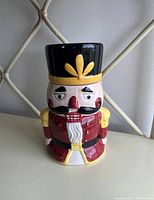 Front view of a nutcracker cookie jar showing detailed facial features and attire, with a small chip on the hat.