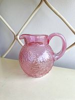 Front view of vintage pink mini glass pitcher showing the round textured body, clear spout, and handle.
