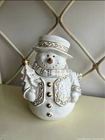 Front view of one snowman cookie jar showing white ceramic body and gold accent details on hat, buttons, and tree decoration.