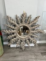 Full view of the starburst mirror showing ornate leaf-shaped frame and central round mirror reflecting surroundings