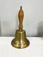 Full view of vintage large brass bell showing its shape, size, brass body and wooden handle.
