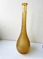Full view of amber genie bottle decanter with hobnail texture against a plain background