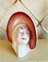 Front angled view showing the lady head face with painted wide brim hat in gradient red and white.