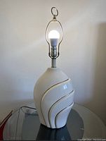 Full view of the vintage lacquered gloss finish table lamp showing cream ceramic base with gold accents, harp and finial for lampshade.