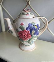 Front angle showing floral design with red rose, blue pansy, and butterfly lid.