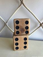 Two large wooden dice stacked one on top of the other showing the natural wood grain and black pips.