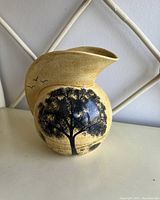 Front view of yellow ceramic vase showing tree and bird silhouette design and speckled yellow finish.
