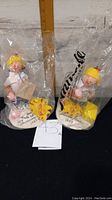 Two Annalee 10th Anniversary Edition dolls in original plastic packaging, showing front view with yellow hats and white outfits