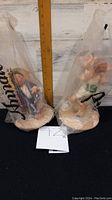 Two Annalee Dolls still sealed in original plastic bags, standing on round bases with a ruler for size reference.