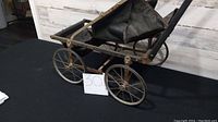 Side view of the antique folding doll stroller showing metal wheels, fabric seating, and foldable handle