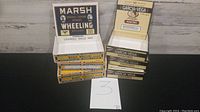 Photo showing 6 cardboard cigarette boxes: three Marsh Wheeling and three Garcia Vega Miniatures, displayed on a surface with a number 3 card nearby.