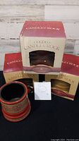 Four ceramic candle crocks displayed with three in their red and beige branded boxes and one out of box showing design and power cord.
