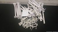 Wide shot showing multiple white display brackets and hooks piled together on a black surface.