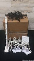 Overview photo showing more than 40 black and white display brackets arranged on and around two cardboard boxes including multiple styles.
