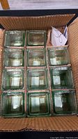 Box containing 11 square green tint glass votive holders arranged in rows.